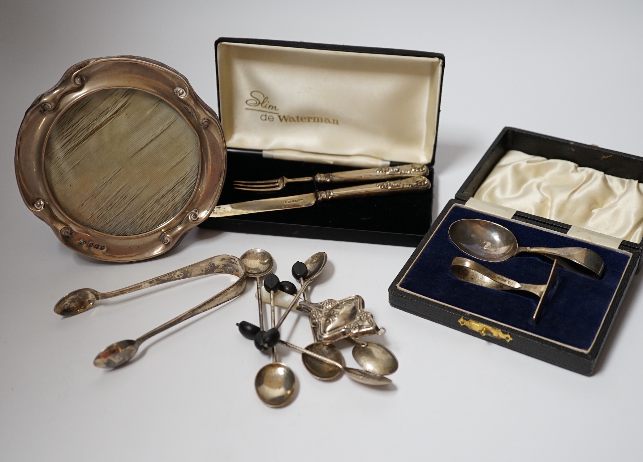 A cased silver christening spoon & pusher, a Georgian silver christening knife and fork, six silver bean end coffee spoons, a child's silver rattle, silver sugar tongs and a silver mounted photograph frame, Birmingham, 1